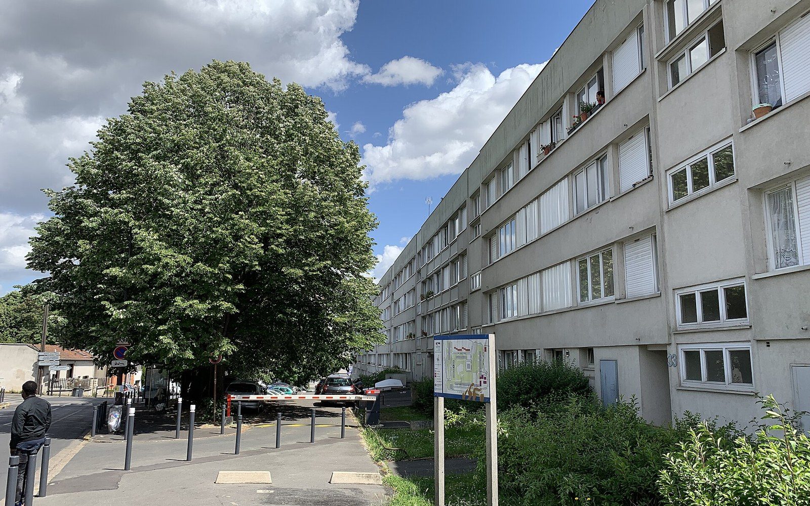 A Seine-Saint-Denis street with a person walking, ordinary residential blocks, daylight