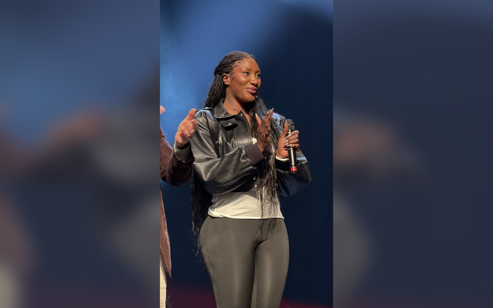 Woman with long braided hair holds a microphone while speaking on stage