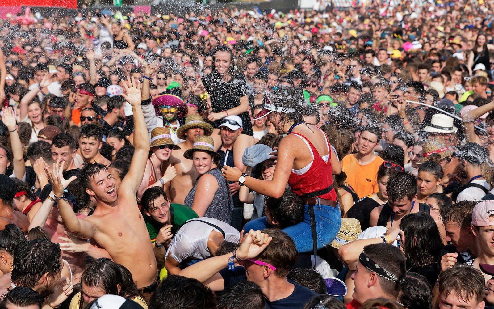 A dense crowd of festivalgoers dances and sprays water under bright sunlight at Les Vieilles Charrues