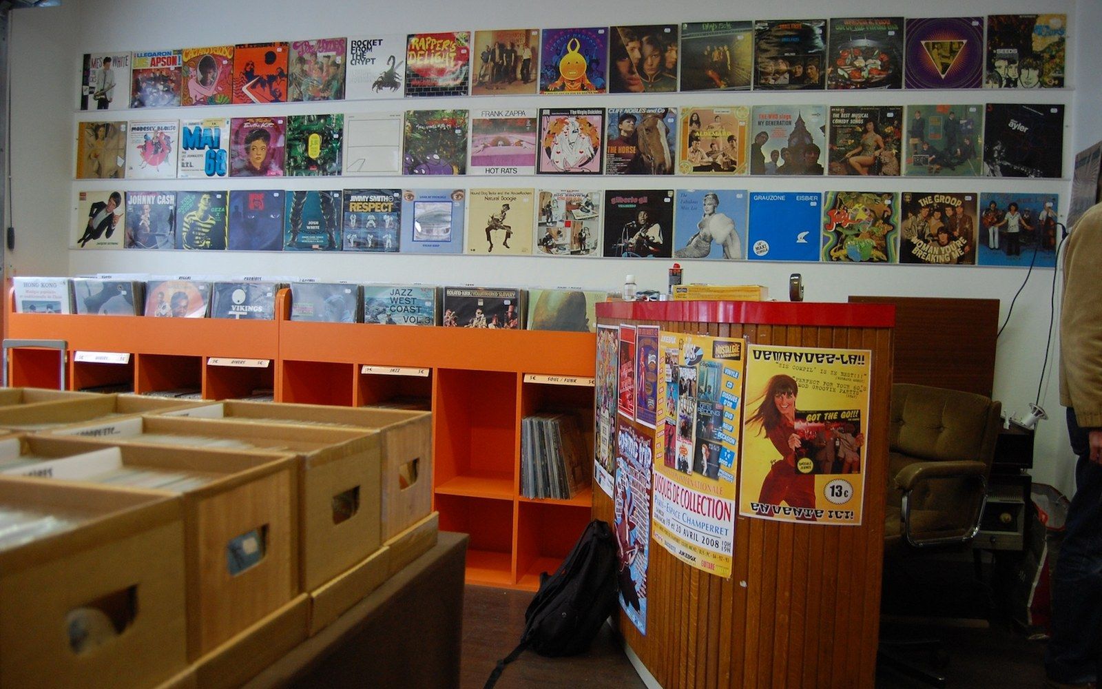 Rows of vinyl album covers mounted on a record shop wall above orange storage bins