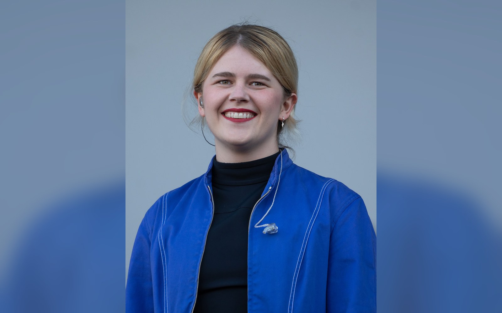 Woman with blonde hair smiling in a blue jacket over a black turtleneck